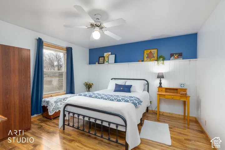 Recessed window with wood trim, wood-finish flooring, white ceiling fan with integrated lighting, and a white paneled accent wall