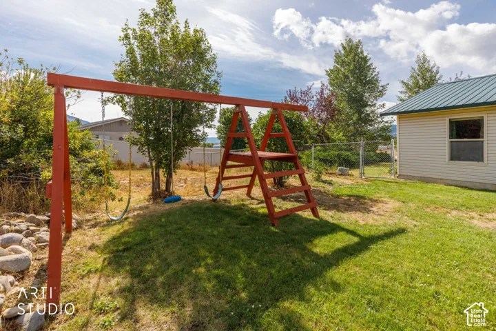 Grassed yard area featuring a wooden swing set, mature trees, and a chain-link fence