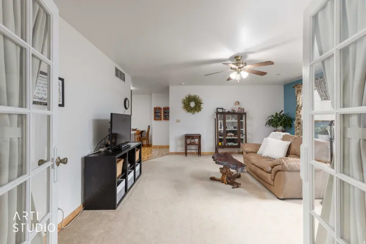 French doors with glass panes open to a carpeted living space with a ceiling fan