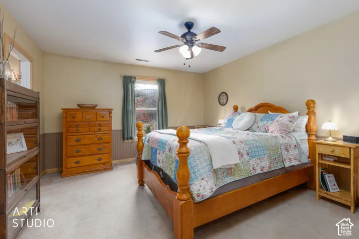 Neutral wall paint, ceiling fan with integrated lighting, window with drapes, and paneled wall accent