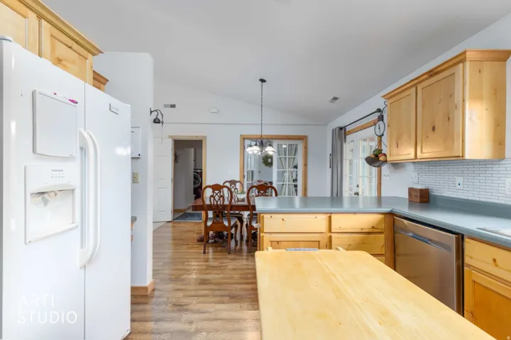 Vaulted ceilings, wood-finish flooring, light wood cabinetry, white subway tile backsplash, and stainless steel appliances