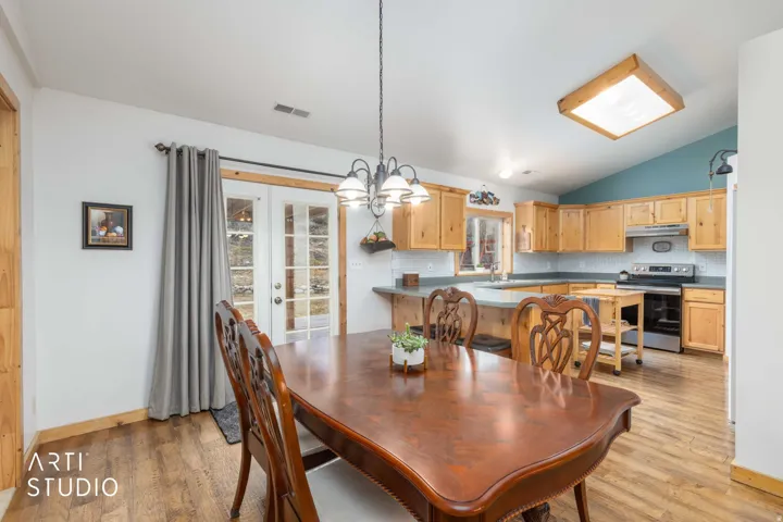 Open-concept living space with wood-finish flooring, natural wood cabinetry, stainless steel appliances, and a tiled backsplash