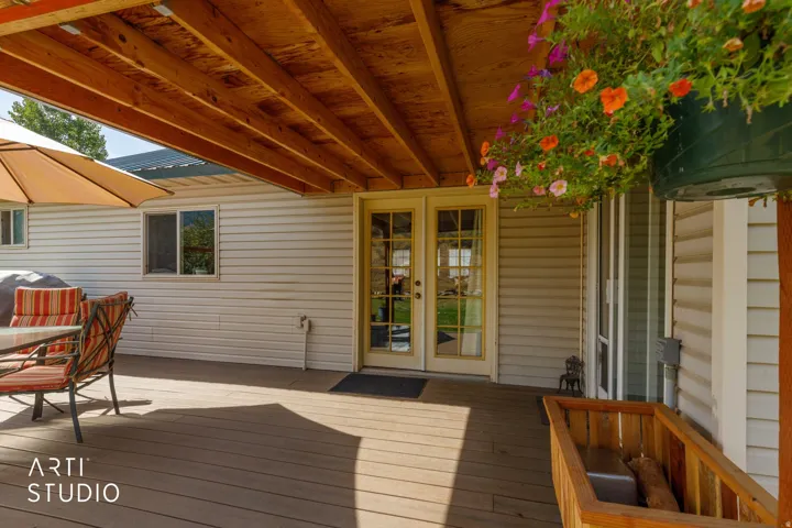 Expansive outdoor deck featuring a covered area with exposed wood beams, white siding, and double glass-paned doors