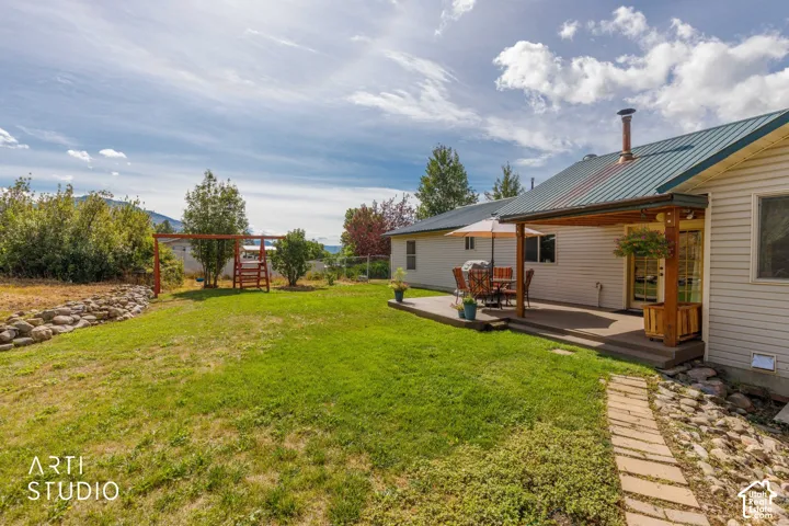Expansive backyard featuring a green lawn, covered patio, and a stone-lined pathway