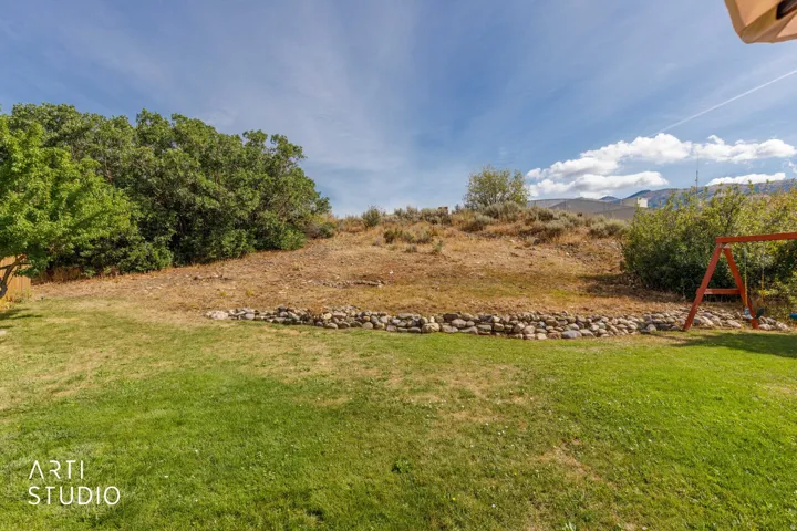 Expansive backyard featuring a manicured lawn, established trees, and a natural rock retaining wall