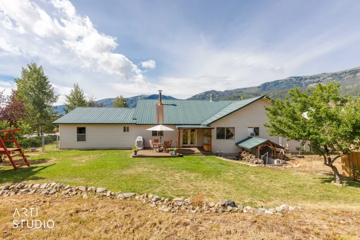 Expansive backyard featuring a green metal roof, a wood deck, and mountain backdrop