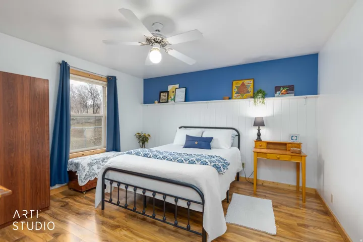 Recessed window with wood trim, wood-finish flooring, white ceiling fan with integrated lighting, and a white paneled accent wall
