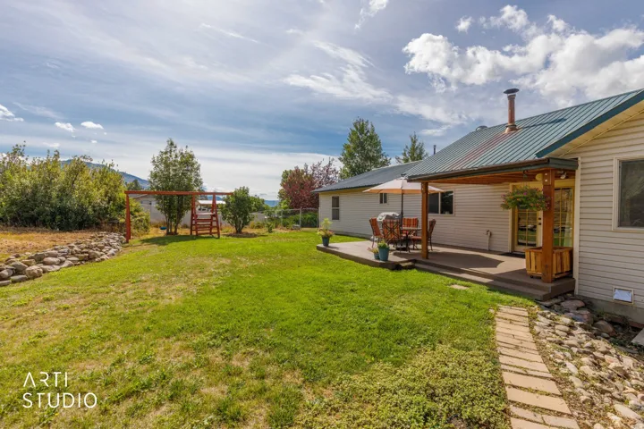 Expansive backyard featuring a green lawn, covered patio, and a stone-lined pathway