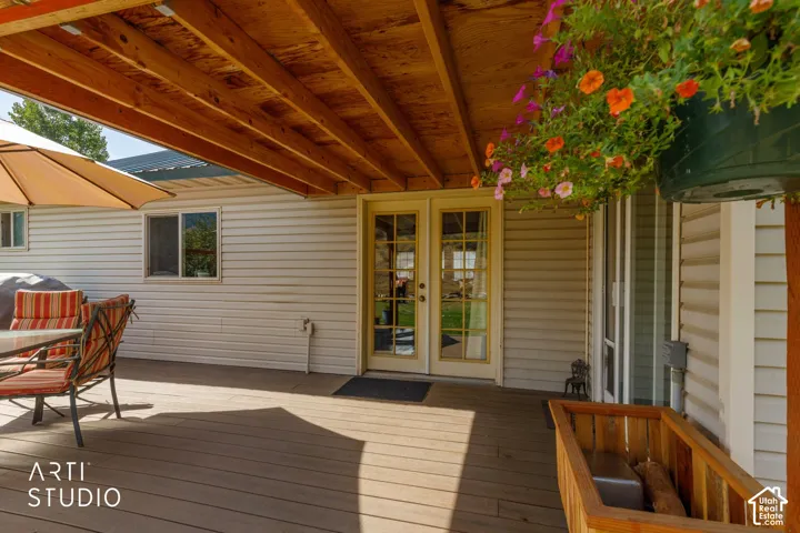 Expansive outdoor deck featuring a covered area with exposed wood beams, white siding, and double glass-paned doors