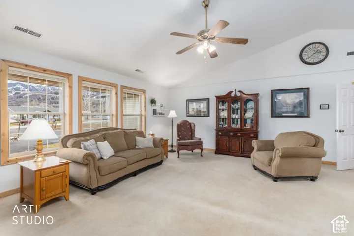 Vaulted ceiling with a ceiling fan, light-toned carpet flooring, multiple windows with natural wood trim, and a built-in display cabinet