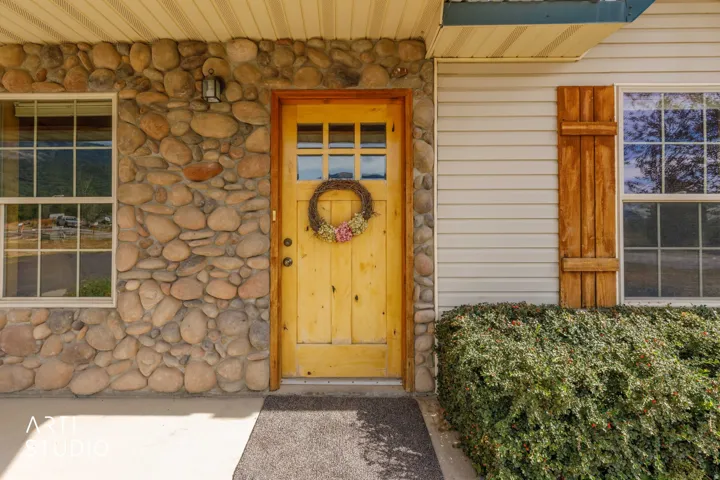 Stone veneer exterior with a paneled wood-finish door, multi-pane windows, and wood-finish shutters