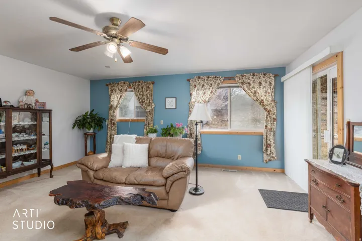 Ceiling fan with integrated lighting, wood-finish window frames, sliding glass door, and wall-to-wall carpeting