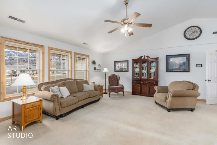 Vaulted ceiling with a ceiling fan, light-toned carpet flooring, multiple windows with natural wood trim, and a built-in display cabinet