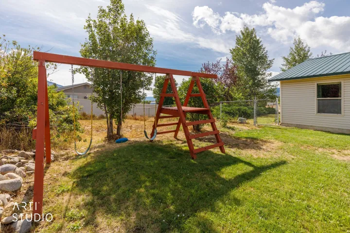 Grassed yard area featuring a wooden swing set, mature trees, and a chain-link fence