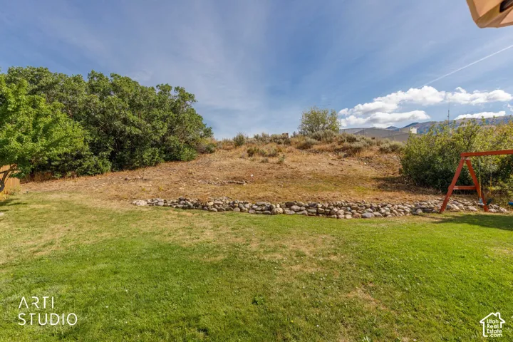 Expansive backyard featuring a manicured lawn, established trees, and a natural rock retaining wall