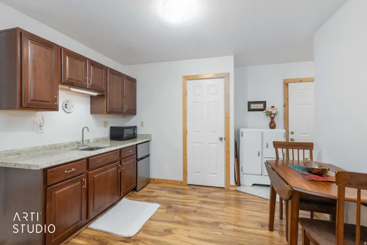 Wood-finish flooring, white walls, wood cabinetry, light-toned countertops, and a stainless steel sink