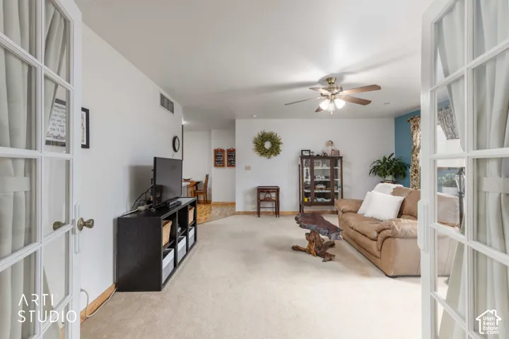 French doors with glass panes open to a carpeted living space with a ceiling fan