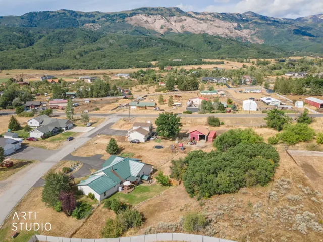 Expansive mountainous backdrop frames a residential area with a single-story property featuring a green roof, a paved patio, and mature landscaping