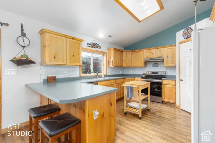 Kitchen featuring light wood cabinetry, a skylight, wood-finish flooring, a stainless steel range, and a tile backsplash