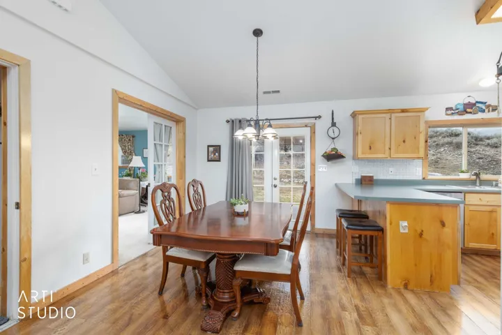 Wood-finish flooring throughout, vaulted ceiling, built-in light wood cabinetry, white tile backsplash, and a breakfast bar