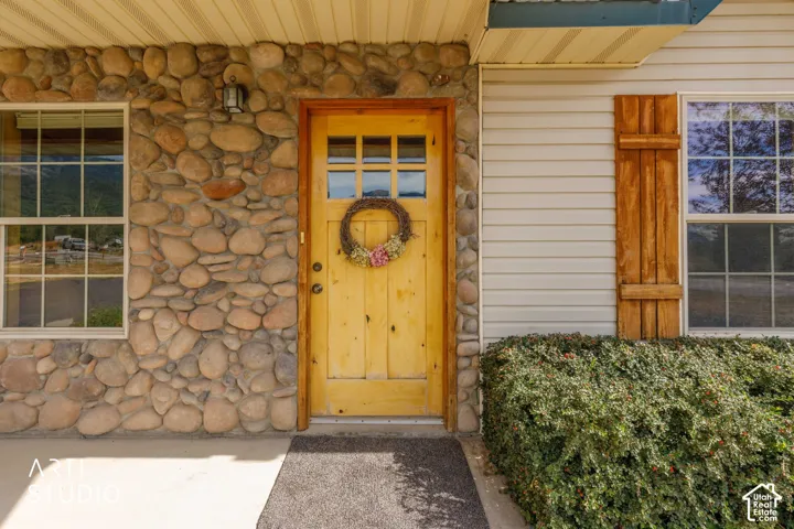 Stone veneer exterior with a paneled wood-finish door, multi-pane windows, and wood-finish shutters