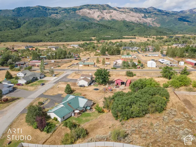 Expansive mountainous backdrop frames a residential area with a single-story property featuring a green roof, a paved patio, and mature landscaping