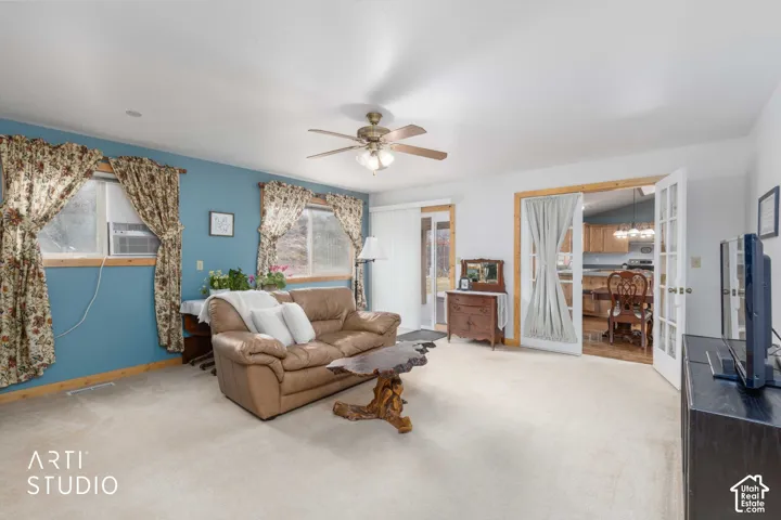 Living area with light-toned carpeting, a ceiling fan with integrated lighting, and multiple windows