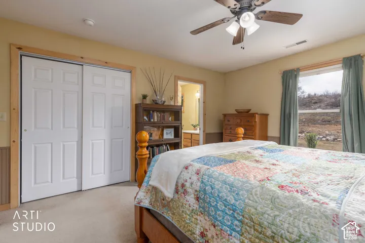Built-in closet with paneled bifold doors, wood trim accents, light-colored carpeting, and a ceiling fan with integrated lighting