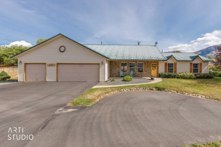 Exterior featuring a metal roof, stone facade accents, decorative window shutters, and a multi-car driveway with an attached garage