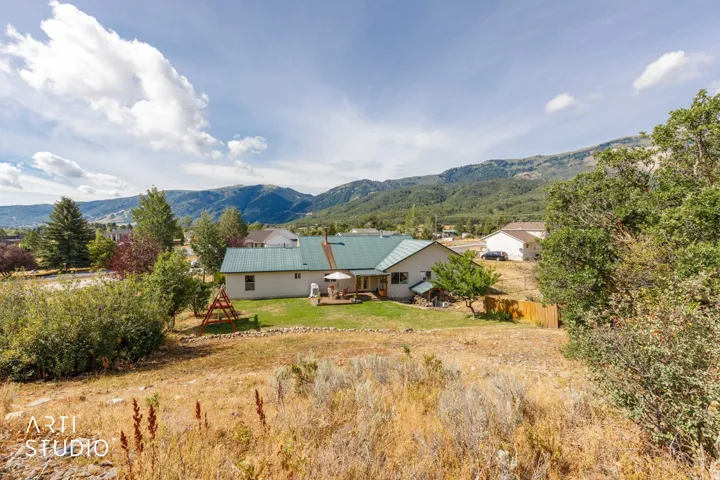 Mountain backdrop, expansive lot, rear deck, green metal roof, mature trees