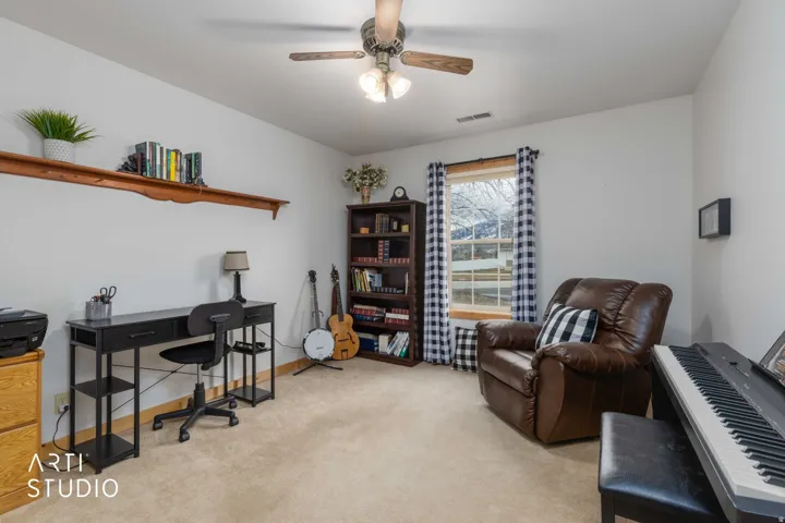 Carpeted room with a ceiling fan, wall-mounted shelving, and window with exterior scenery