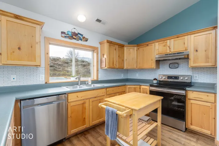 Kitchen featuring natural wood-finish cabinetry, stainless steel appliances, light-toned backsplash, and wood-finish flooring