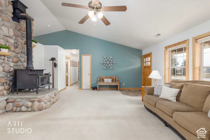Vaulted ceiling, stone-clad wood-burning stove, large windows with natural wood trim, and a ceiling fan