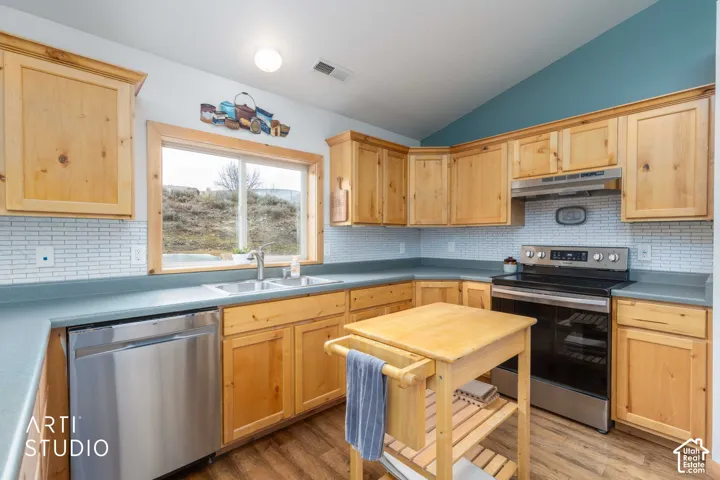 Kitchen featuring natural wood-finish cabinetry, stainless steel appliances, light-toned backsplash, and wood-finish flooring