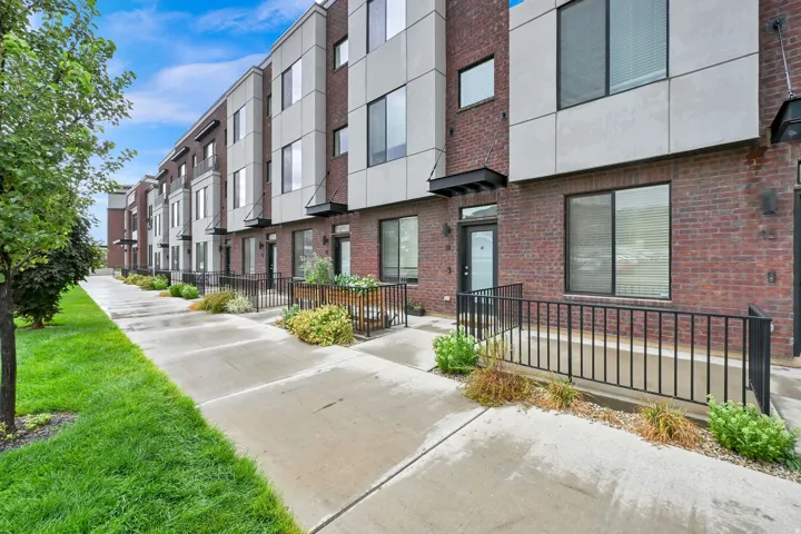 Modern townhome exterior featuring brick and paneling, a front entry with an awning, and a private patio space enclosed by black railings