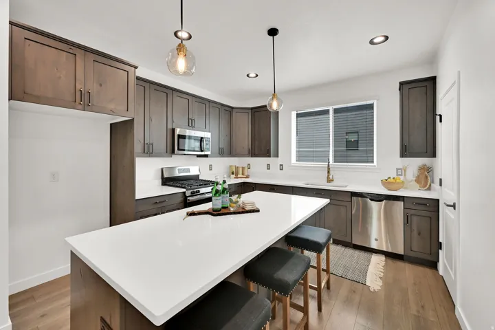 Kitchen featuring a white countertop island, wood-finish flooring, stainless steel appliances, dark wood cabinetry, and recessed lighting