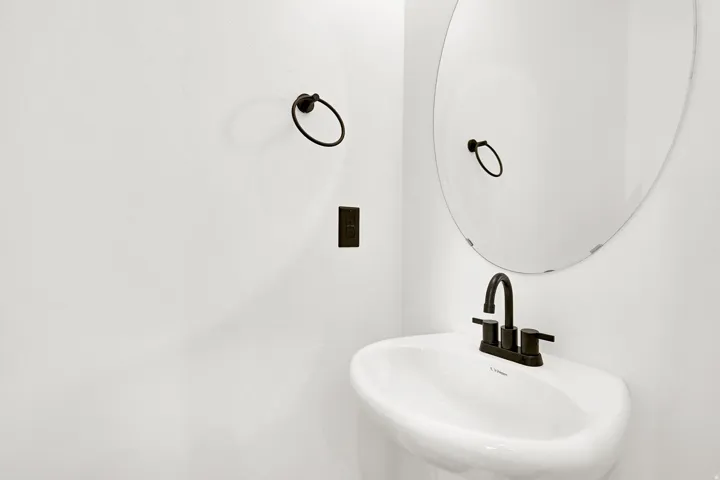 1/2 bath with Pedestal sink with dark bronze faucet, round mirror, and wall-mounted towel ring