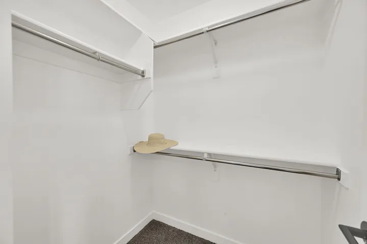 Spacious closet with multiple shelving units and chrome hanging rods, featuring light-colored walls and carpet flooring