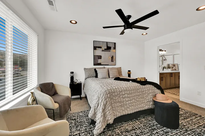 Recessed lighting, ceiling fan, large window with blinds, carpeted flooring, and an adjoining bathroom with a vanity