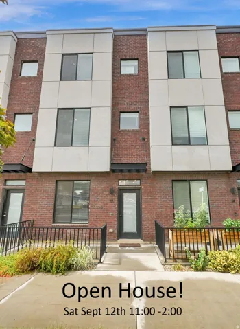 Modern multi-story facade featuring brick and paneling, dark-framed windows, and a glass-paneled entry door