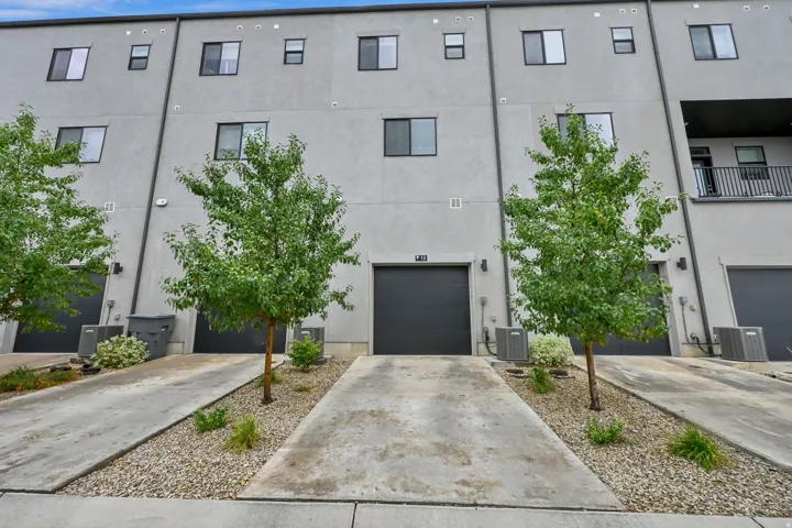 Contemporary townhome exterior with gray stucco siding, multiple windows, attached garages with dark doors, and small balcony