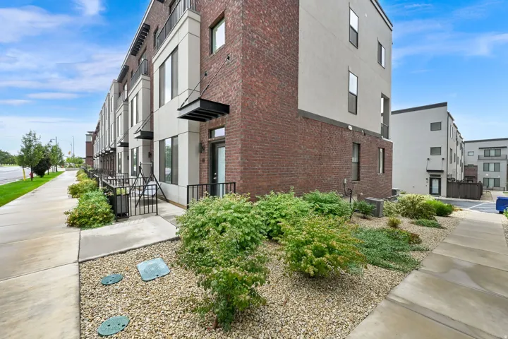 Modern townhome exterior featuring brick and stucco siding, a black metal entry awning, and a private patio with metal railings