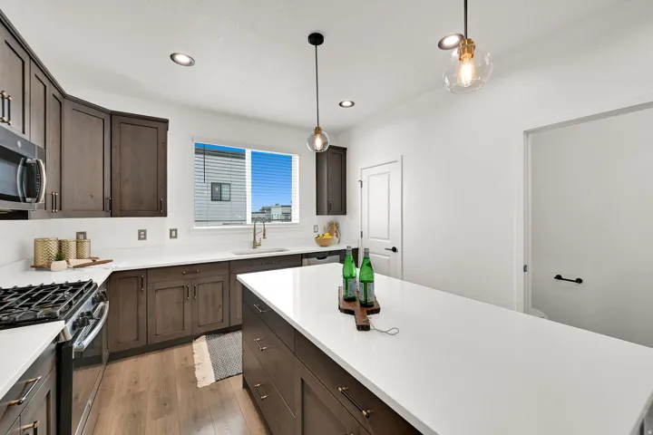 Kitchen featuring dark wood-finish cabinetry, white countertops, stainless steel appliances, and a central island with pendant lighting