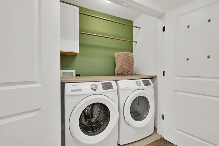 Dedicated laundry area featuring a wood-finish countertop, white cabinetry, and wall-mounted hanging rods
