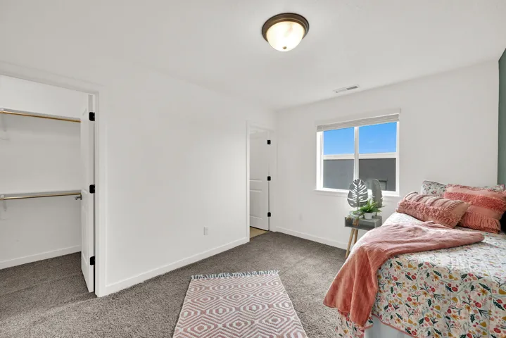 Neutral wall color, carpet flooring, window with blinds, ceiling light fixture, and an open closet with shelving and hanging rods