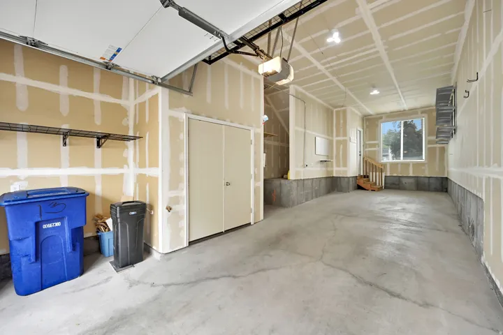 Concrete flooring with an automatic garage door opener, a window for natural light, built-in shelving, and a separate access door with wooden stairs