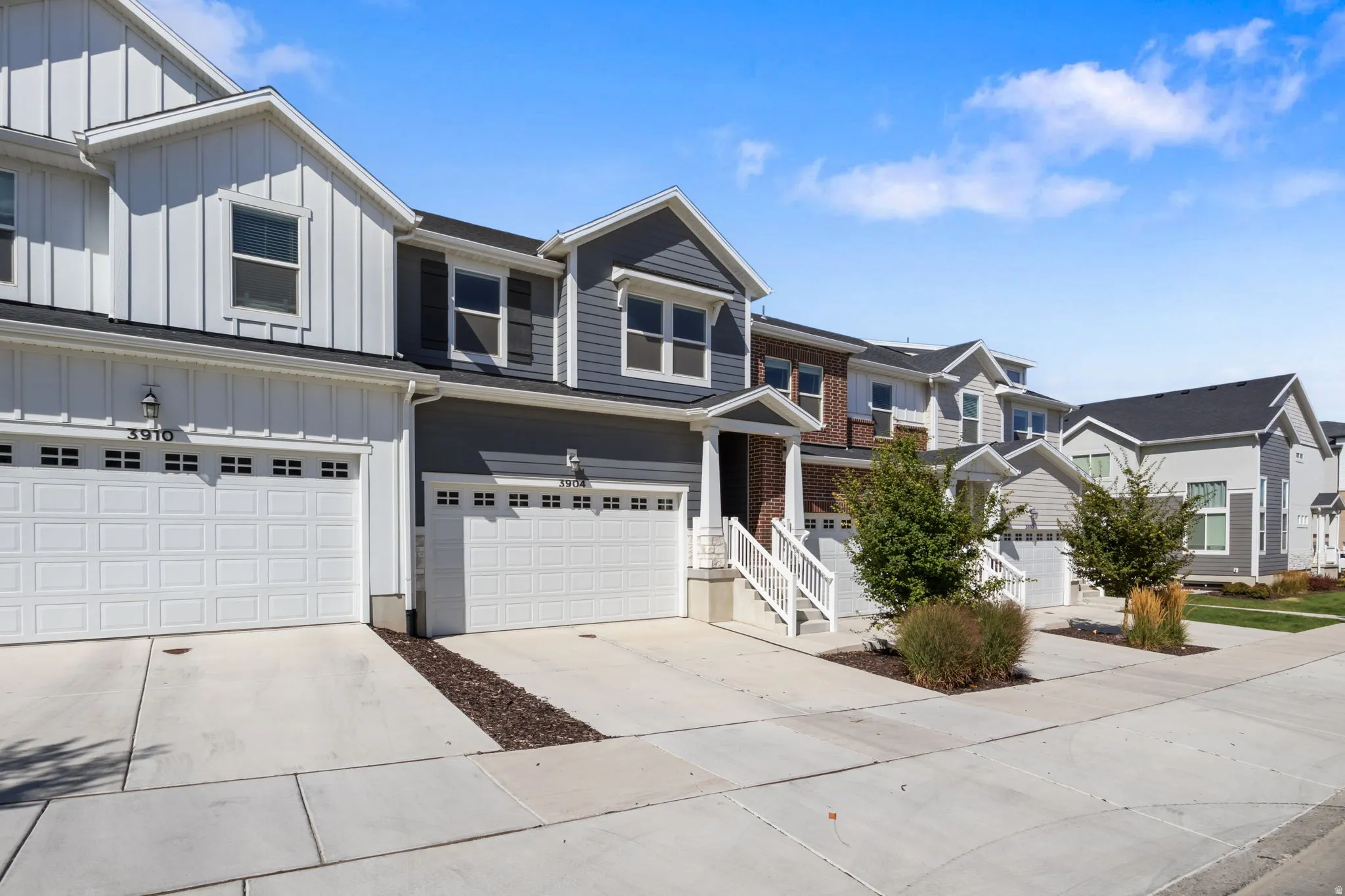 Contemporary townhomes featuring a combination of vertical and horizontal siding, attached two-car garages, mature landscaping, and concrete driveways