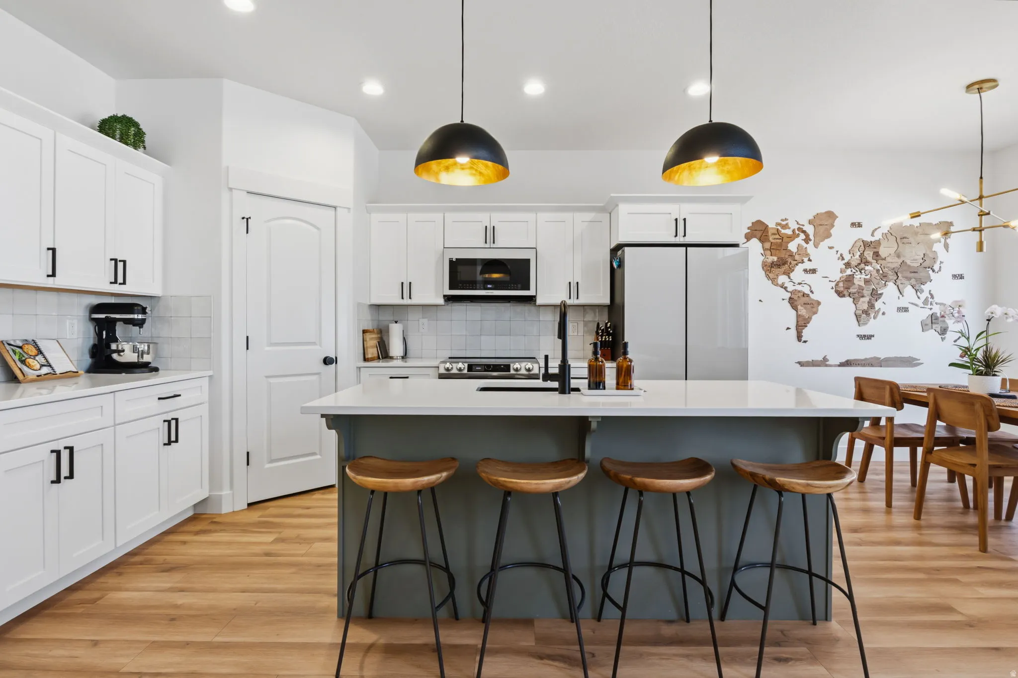 White cabinetry with matte black hardware, light-toned wood-finish flooring, island with light countertop, built-in microwave, and stainless steel refrigerator