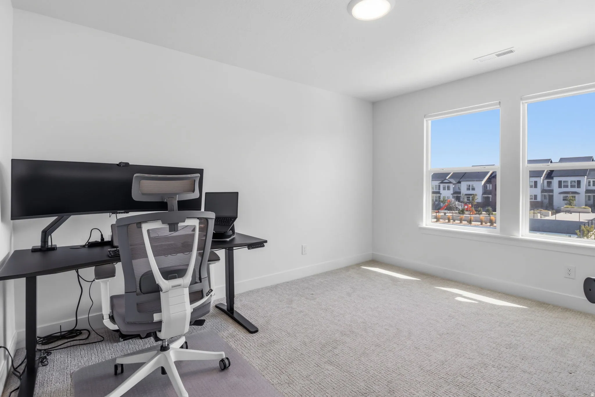 Recessed ceiling lighting, two large windows, light neutral wall paint, and light neutral carpeting