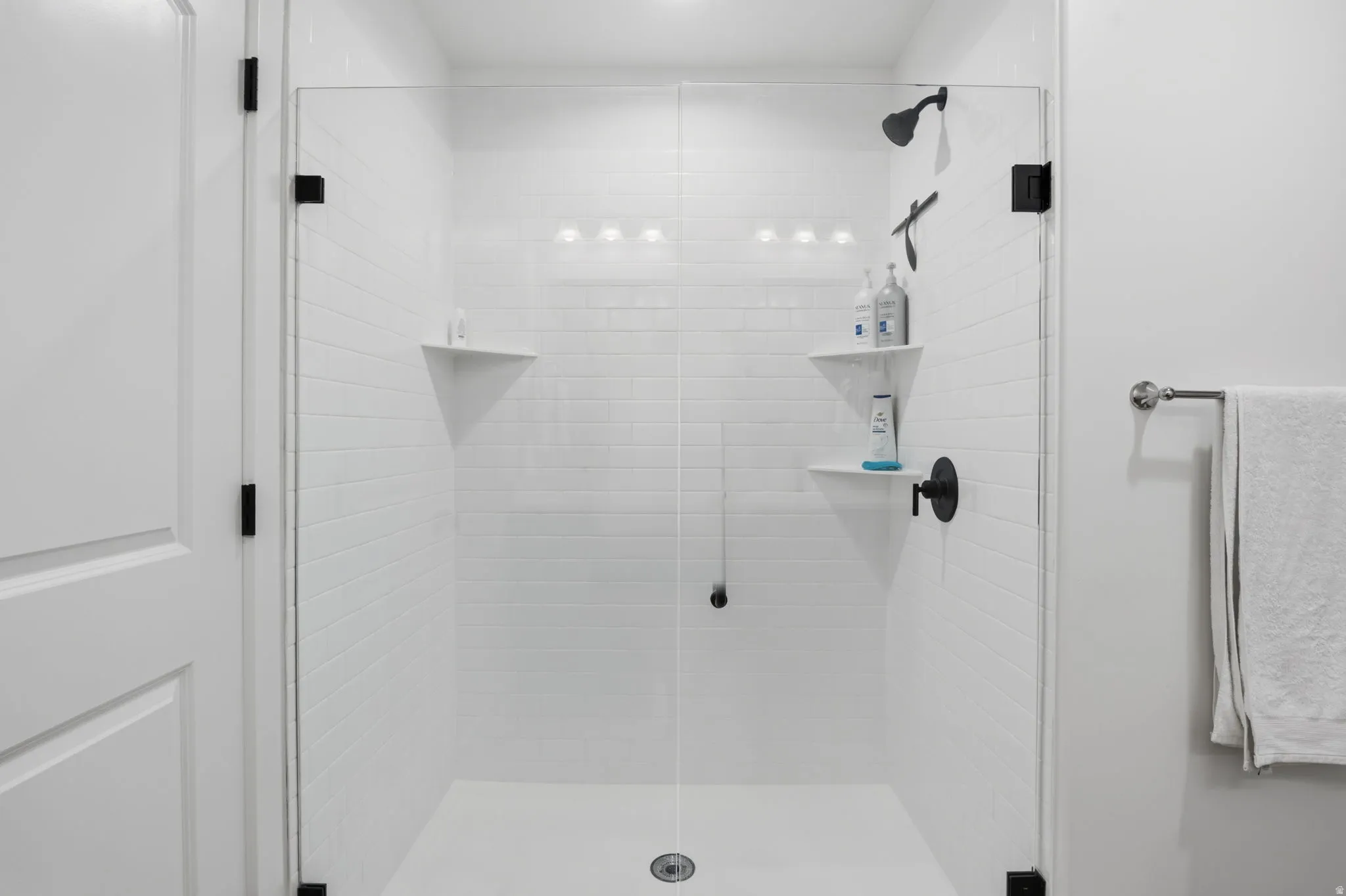 Glass-enclosed shower with white subway tile, a matte black shower head, and built-in shelving